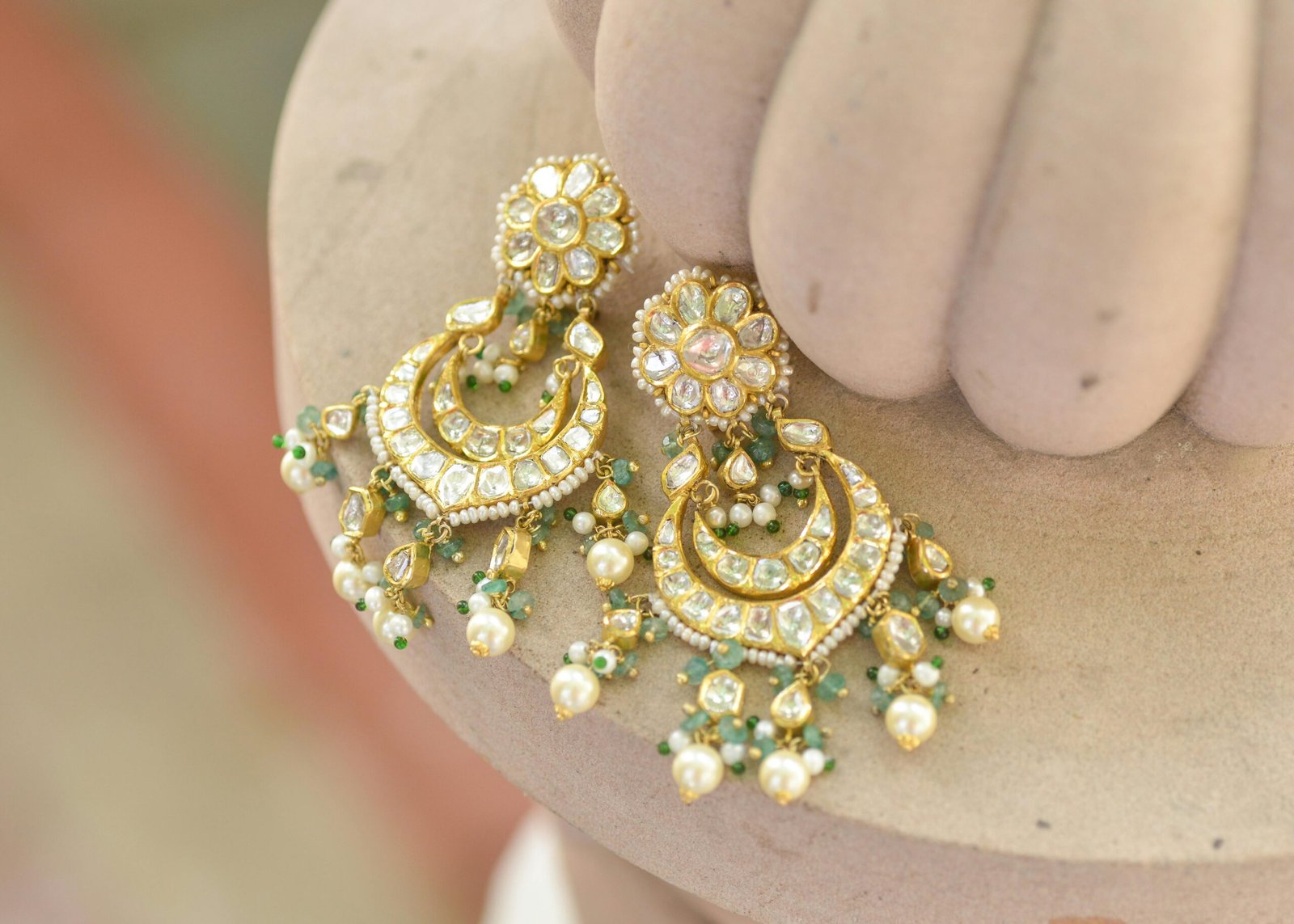 Close-up of exquisite gold earrings embellished with pearls and green beads, showcasing intricate craftsmanship.